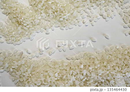 Close-up of high-quality raw white rice grains spread on a white surface with a central empty space for text. Perfect for food, cooking, and health-related designs 135464430