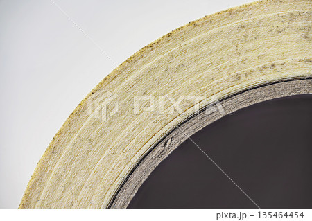 A detailed macro shot showing the side profile and layered texture of a roll of paper masking tape on a cardboard core, highlighting its industrial and craft use 135464454