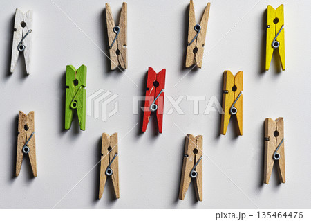 Top view of a group of seven wooden clothespins in green, red, yellow and natural colors on a white textured background, illustrating leadership and individuality concepts 135464476
