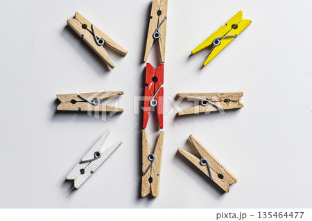 A red clothespin in the center of a circle made of wooden, yellow, and white clothespins, symbolizing leadership and uniqueness on a white background 135464477