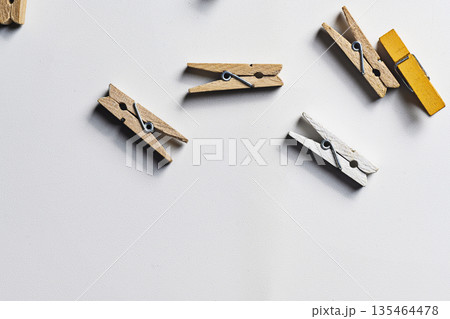A collection of small natural, white, and yellow wooden clothespins scattered on a white surface, providing ample copy space for text. Perfect for laundry, craft, or office themes 135464478