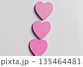 A vertical arrangement of three small, bright pink wooden heart shapes centered on a textured white surface, perfect for Valentine's Day or romantic themes 135464481