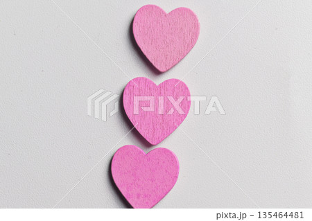 A vertical arrangement of three small, bright pink wooden heart shapes centered on a textured white surface, perfect for Valentine's Day or romantic themes 135464481