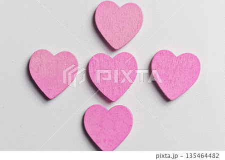 Five small pink wooden hearts arranged in a cross pattern on a white textured background. A minimal and romantic composition perfect for Valentine's Day, love, and greeting card designs 135464482