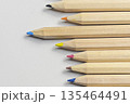 A high-angle, close-up shot of a group of natural wood colored pencils with various colored tips, arranged in a row on a white textured paper background 135464491