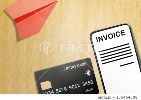 Smartphone displaying an online invoice next to a credit card and red paper plane on a wooden surface. Concept of digital billing, travel expenses, and mobile payment solutions 135464509