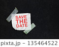 A conceptual image featuring the text 'Save the Date' in red on a crumpled piece of white paper, taped to a dark textured background with translucent tape. Great for event reminders 135464522