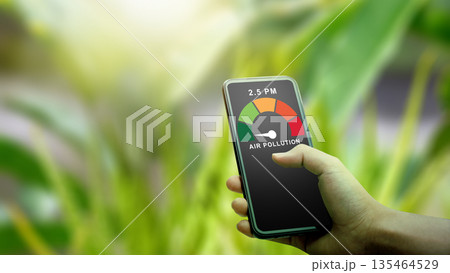 A person checks high air pollution levels and PM2.5 on a mobile app while outdoors. The digital gauge shows poor air quality against a blurred green plant background A person checks high air pollution levels and PM2.5 on a mobile app while outdoors. The digital gauge shows poor air quality against a blurred green plant background 135464529