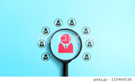 Magnifying glass focusing on a red person icon among several black icons on a blue background, representing talent search, hiring, and selection in human resources Magnifying glass focusing on a red person icon among several black icons on a blue background, representing talent search, hiring, and selection in human resources 135464536