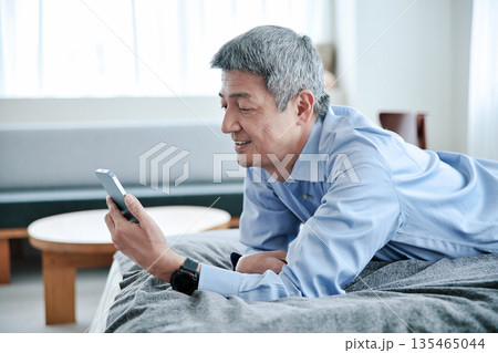 ベッドに寝転んでスマホを見るシニア男性 ベッドに寝転んでスマホを見るシニア男性 135465044
