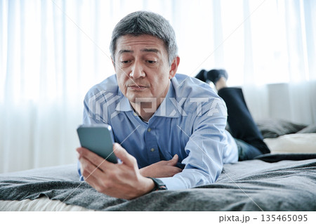 ベッドに寝転んでスマホを見るシニア男性 ベッドに寝転んでスマホを見るシニア男性 135465095