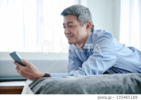 ベッドに寝転んでスマホを見るシニア男性 135465189
