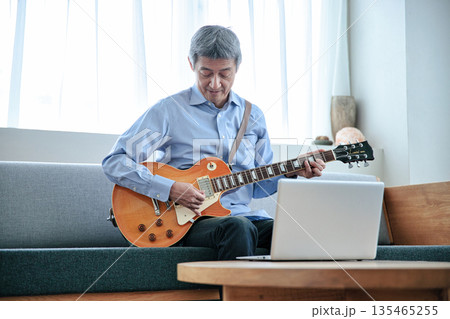 ノートパソコンでギターのオンラインレッスンを受けるシニア男性 135465255