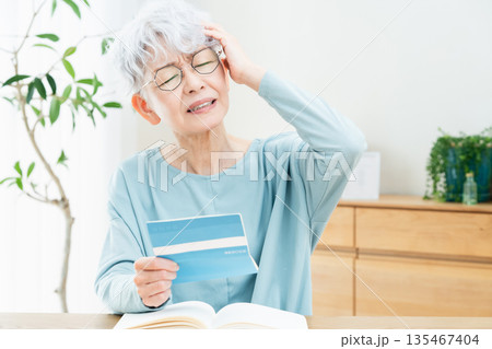 預金通帳を見て考えるシニア女性 預金通帳を見て考えるシニア女性 135467404