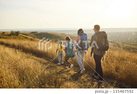 Family hike on trail in sunny autumn nature, back view of hikers walk in golden hour 135467592