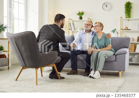 Senior couple shaking hands with real estate agent after signing agreement at home 135468377