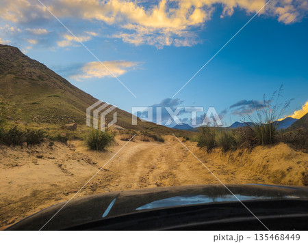 View on dirt road in mountainous landscape at twilight from car driver perspective View on dirt road in mountainous landscape at twilight from car driver perspective 135468449