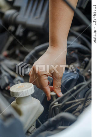 Close up of a hand of woman pulling an engine oil dipstick to inspect oil level Close up of a hand of woman pulling an engine oil dipstick to inspect oil level 135468511