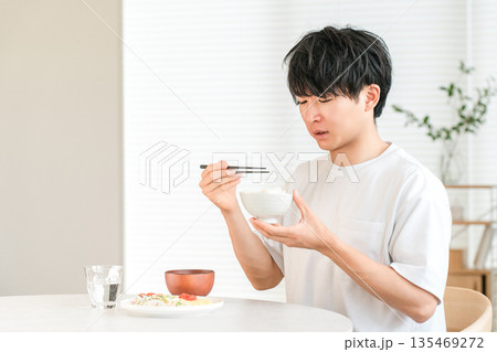 自宅のダイニングで美味しくない白米を食べる若いアジア人男性(輸入米,古米,米不足) 自宅のダイニングで美味しくない白米を食べる若いアジア人男性(輸入米,古米,米不足) 135469272