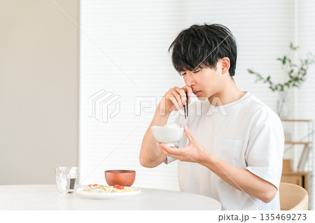 自宅のダイニングで美味しくない白米を食べる若いアジア人男性(輸入米,古米,米不足) 自宅のダイニングで美味しくない白米を食べる若いアジア人男性(輸入米,古米,米不足) 135469273