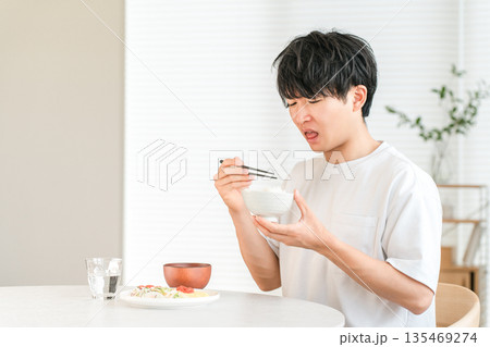 自宅のダイニングで美味しくない白米を食べる若いアジア人男性(輸入米,古米,米不足) 自宅のダイニングで美味しくない白米を食べる若いアジア人男性(輸入米,古米,米不足) 135469274