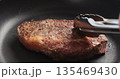 Closeup shot of man hands flip ribeye steak on non stick pan with steel tongs 135469430