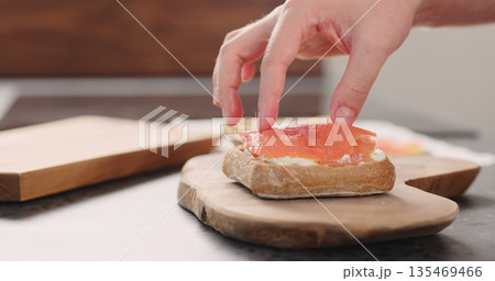 man hands put smoked salmon on ciabatta with cream cheese to make a sandwich on wood board 135469466