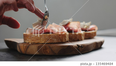 Slow motion man add ricotta to slice of ciabatta with fig marmalade and pancetta Slow motion man add ricotta to slice of ciabatta with fig marmalade and pancetta 135469484