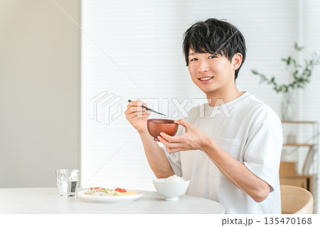 家のダイニングテーブルでお味噌汁を飲む若いアジア人男性 135470168