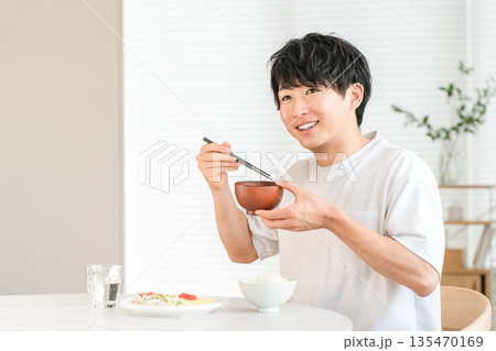 家のダイニングテーブルでお味噌汁を飲む若いアジア人男性 家のダイニングテーブルでお味噌汁を飲む若いアジア人男性 135470169
