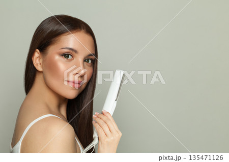 Cute woman brunette with long straight smooth hairstyle using hair straightener iron Cute woman brunette with long straight smooth hairstyle using hair straightener iron 135471126
