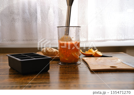 Mixing sea buckthorn and orange in a jar with immersion blender on a wooden table near the window 135471270