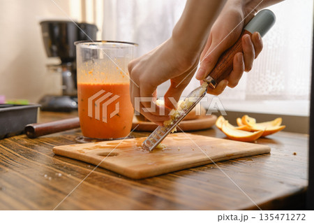 Grating fresh ginger on a wooden cutting board in a kitchen Grating fresh ginger on a wooden cutting board in a kitchen 135471272