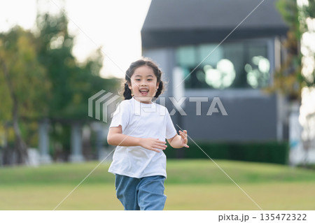 Happy child running in the park on a sunny day, enjoying outdoor activity and carefree childhood moments with bright green grass and trees in the background 135472322