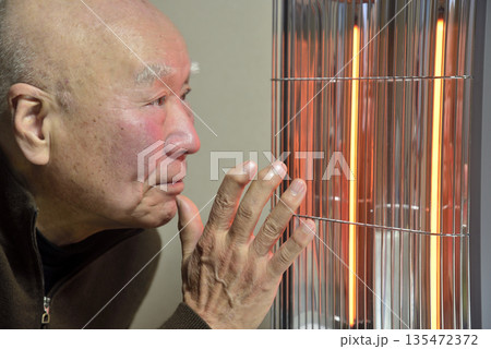 電気ストーブで暖をとる老人 135472372