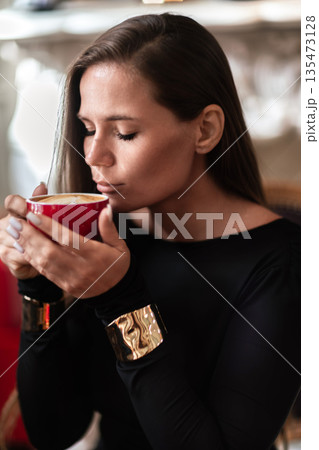 Woman Coffee Bracelet: Brunette drinks coffee indoor, morning light, to enjoy the aroma and taste. Woman Coffee Bracelet: Brunette drinks coffee indoor, morning light, to enjoy the aroma and taste. 135473128