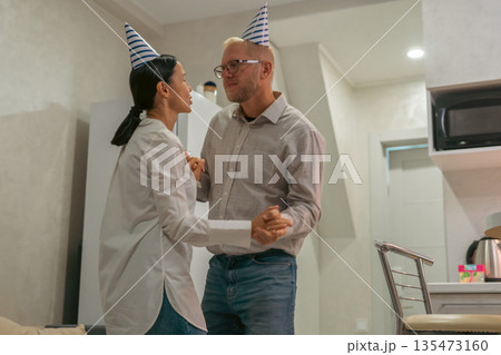 Couple Dancing Party Hats Apartment: Intimate birthday celebration; man woman slow dance; home interior setting. 135473160