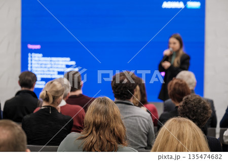Presenter speaks to attentive audience during conference with large blue screen backdrop Presenter speaks to attentive audience during conference with large blue screen backdrop 135474682