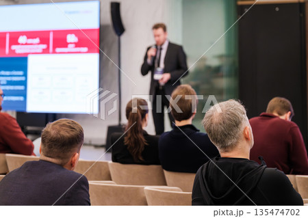 Business conference scene with speaker presenting to attentive audience in a modern meeting hall Business conference scene with speaker presenting to attentive audience in a modern meeting hall 135474702