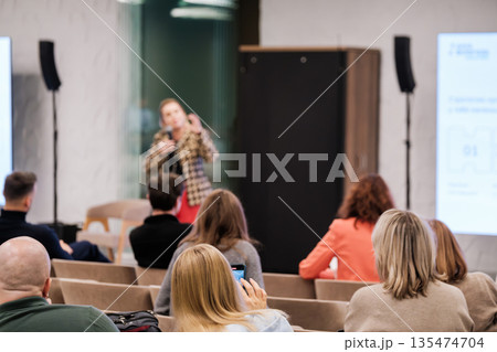 Speaker presents to seated audience during a conference style presentation in a modern room Speaker presents to seated audience during a conference style presentation in a modern room 135474704