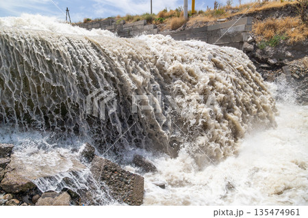Powerful water splashing against concrete structure outdoors Powerful water splashing against concrete structure outdoors 135474961