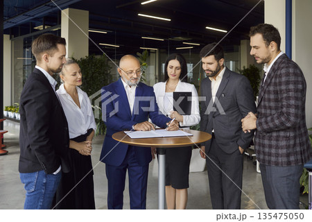 Business team signing contract during standing on meeting in modern office Business team signing contract during standing on meeting in modern office 135475050