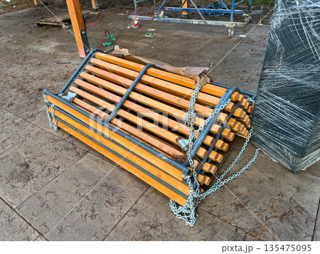 A stack of wooden sleds secured with chains, resting on a concrete surface. The sleds are made of light-colored wood and are neatly arranged. A stack of wooden sleds secured with chains, resting on a concrete surface. The sleds are made of light-colored wood and are neatly arranged. 135475095