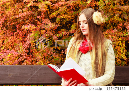 Woman relaxing in autumnal park reading book 135475183