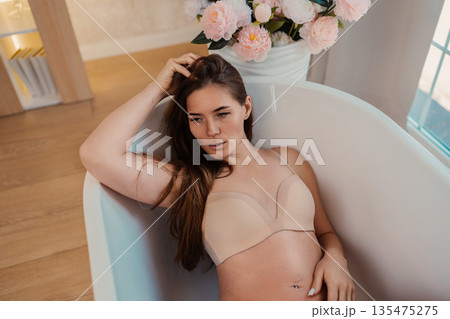 Woman bathtub relaxation, young adult lying in white tub enjoying self-care moment with pink flowers 135475275