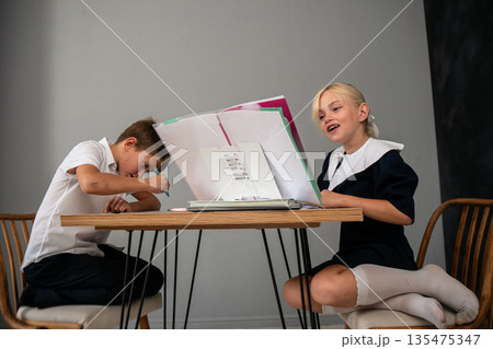 Kids Laptop Learning Online Education - Two children, a boy and a girl, are sitting at a table with a laptop and books. Kids Laptop Learning Online Education - Two children, a boy and a girl, are sitting at a table with a laptop and books. 135475347