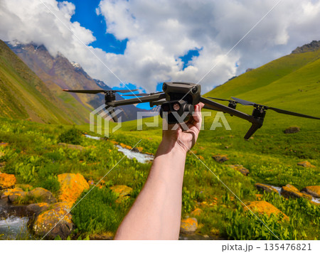 Adult holding drone in mountainous outdoor setting during daytime Adult holding drone in mountainous outdoor setting during daytime 135476821