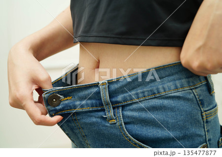 Young Asian woman losing weight wearing loose pants in oversize jeans. 135477877
