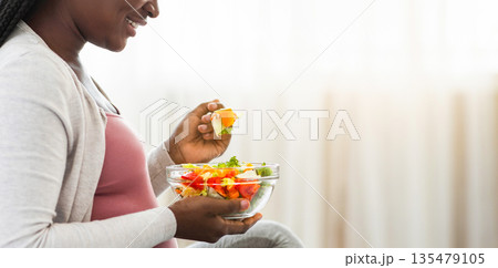 Black Pregnant Lady Enjoying Fresh Vegetable Salat While Sitting On Bed, Enjoying Eating Healthy Nutrition During Pregnancy, Holding Bowl With Organic Meal, Cropped Image, Side View, Panorama 135479105