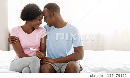 Young black couple will become parents, holding positive pregnancy test and touching each other with foreheads, bedroom interior, empty space. Delighted african american family waiting for baby 135479122